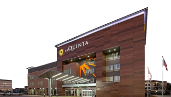 This image shows the exterior of a La Quinta hotel at night with illuminated signage and an entrance canopy. An American flag is seen on the right.