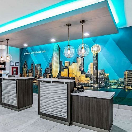 The image shows a modern hotel reception area with two desks, pendant lights, and a mural of a city's skyline in the background.