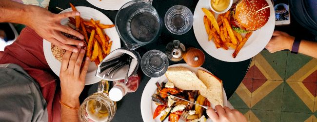 Four people are seated around a table enjoying burgers and fries, alongside drinks, cutlery, and bowls of sauce.