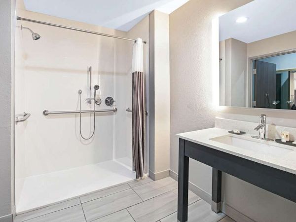 A modern bathroom features a spacious walk-in shower with a curtain, grab bars, and a large vanity with a sink and mirror on the right.