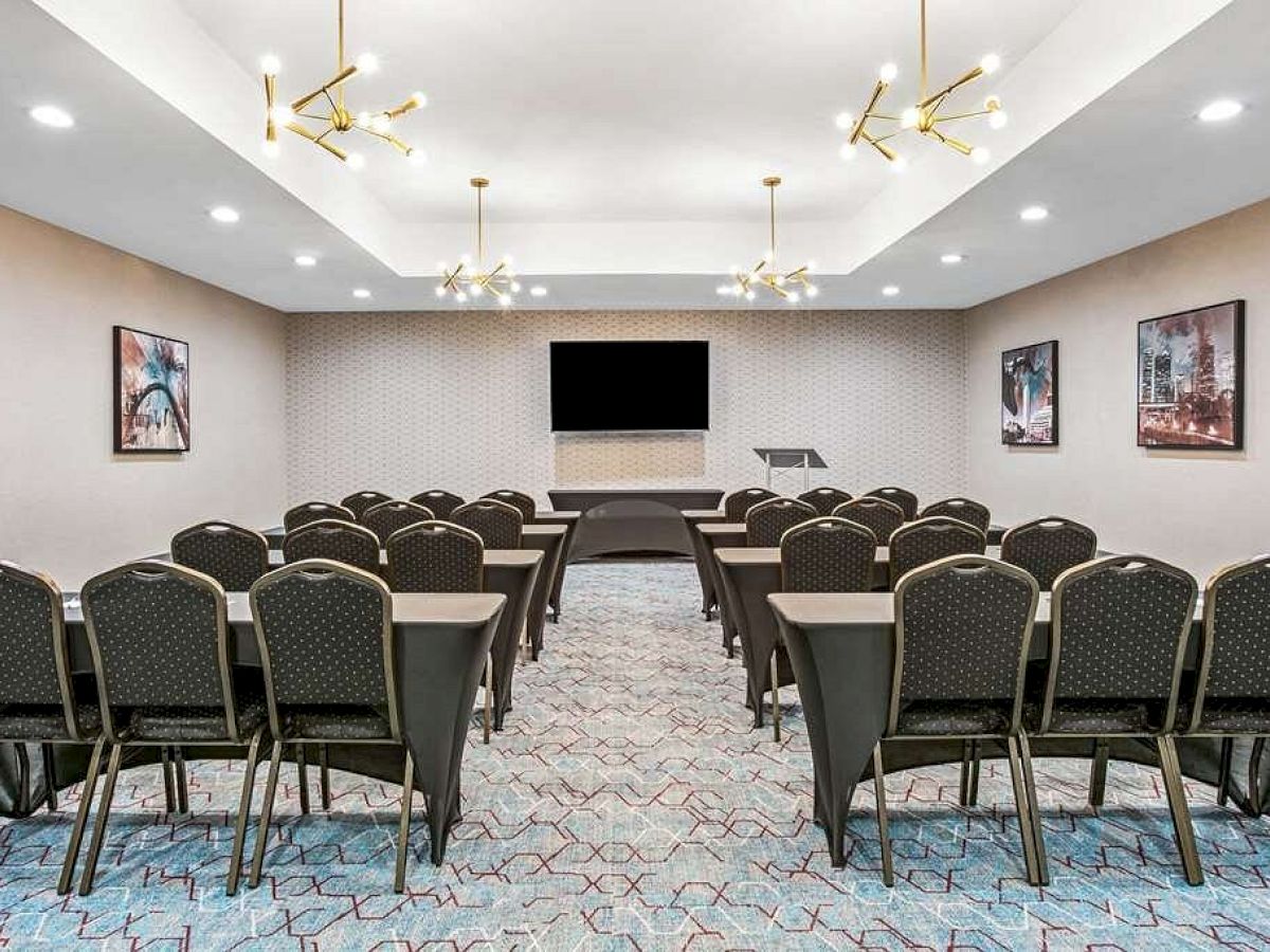 A modern conference room with rows of chairs, a projector screen, and framed artwork on the walls. The room features elegant lighting.